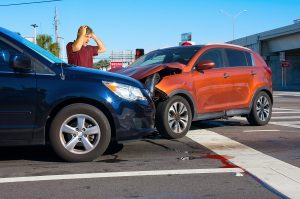 Two cars have crashed wrecked into each other at intersection with very upset man driver looking at the severe damage with wrong way sign in background. If he is driving for work, his employer needs hired and non owned auto insurance. 