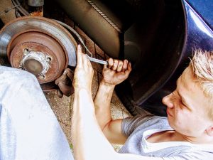 Car mechanis working on the frame of a car near a wheel. 