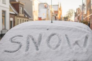 The word snow written on the back window of a car during a Winter Storm. 